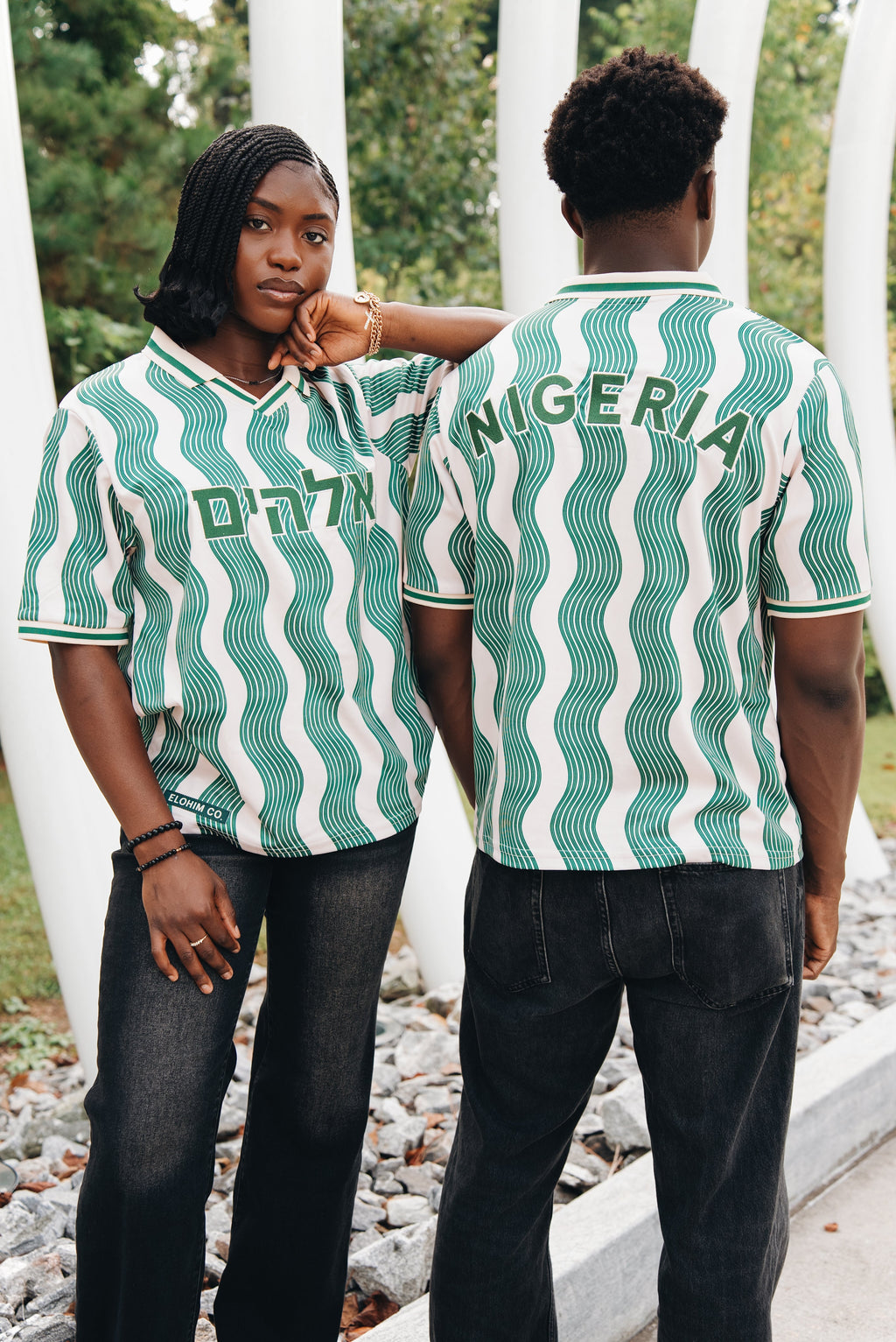 Heritage Jersey — two models wearing the jersey in cream/green wave pattern with Hebrew Elohim lettering, under an arch structure