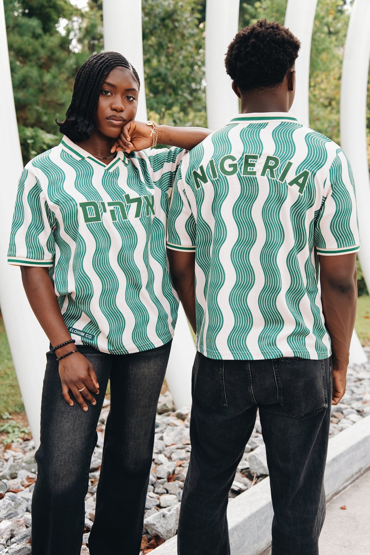 Heritage Jersey — two models wearing the jersey in cream/green wave pattern with Hebrew Elohim lettering, under an arch structure